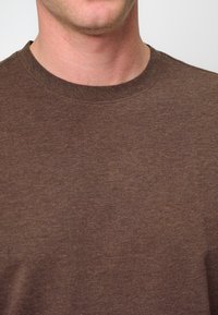 T-shirt marrone a maniche corte con collo a giro, realizzato in morbido tessuto con una trama liscia. Presenta un design semplice e una vestibilità standard.