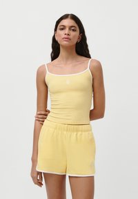 Lys gul ribbet tanktop med hvit kant, parret med matchende shorts med elastisk liv. Har brodert logodetalj.