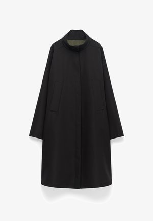 Zwarte jas met hoge kraag, twee voorzakken en lange mouwen. Glad textuur met een rechte silhouet, voorzien van een groene voering.