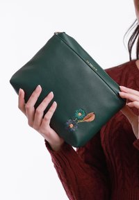 Zelená kožená kabelka na ruku se zlatými akcenty, s květinovou výšivkou v modré, žluté a hnědé barvě. Jemná textura a obdélníkový tvar.