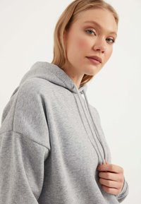 Hellgrauer Hoodie aus weichem Material, mit einer Kordelzugkapuze, lässiger Passform und gerippten Bündchen. Einfaches Design ohne sichtbare Muster.