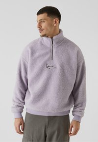 Pullover in pile viola chiaro con collo a mezza zip, polsini e orlo a coste. Presenta un piccolo logo ricamato sul petto.