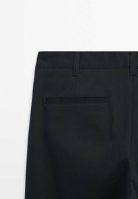 Black trousers featuring a smooth texture, belt loops, and a single back pocket with a rectangular flap closure.