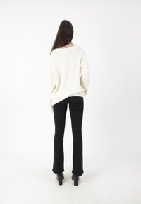 Un pull blanc surdimensionné avec une texture, associé à un pantalon noir évasé ajusté et des bottes à plateforme noires, vu de dos.