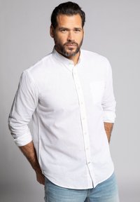 Camisa de lino blanca con dise�ño de botones, presenta mangas largas y un bolsillo en el pecho, combinada con jeans de mezclilla azul claro.
