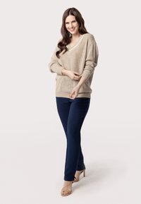 Maglione beige a maglia con scollatura a V, motivo testurizzato e spalle scese, abbinato a pantaloni aderenti blu navy e sandali beige con cinturini.