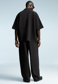 Černá oversized košile a široké kalhoty z texturovaného materiálu. Košile má límeček a krátké rukávy. Jednoduchý design.