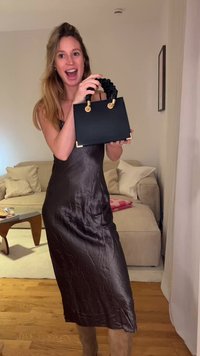 Must käekott struktureeritud disainiga, pehme kangast sang, kuldsed metalldetailid ja ristkülikukujuline, hoitud eredalt valgustatud toas.