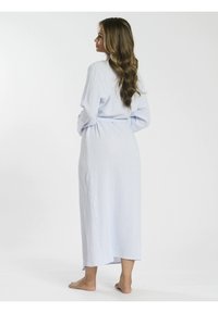 Robe lungo azzurro chiaro, realizzato in tessuto testurizzato. Presenta una vita legata e una fessura laterale, offrendo una silhouette fluida. Stilizzato con dettagli minimali.