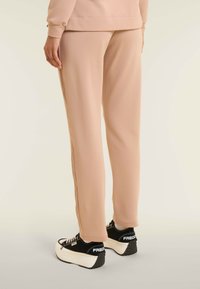 Pantalones de chándal beige en un ajuste relajado con una textura suave, complementados con zapatillas de plataforma negras con acentos blancos y logotipo.