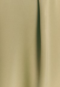 Tkanina z reliefom v svetlo olivno zeleni barvi, s gladko površino in subtilnim sijajem. Material ima fino tkanje, ki ustvarja mehak padec.