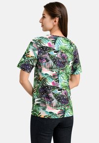 Short-sleeve shirt with a vibrant tropical plant pattern, featuring green and purple leaves on a light background. Round neckline, casual fit.