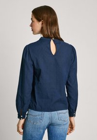 Blusa a maniche lunghe blu navy in tessuto testurizzato, con scollatura rotonda, dettaglio a chiave sul retro e bottoni decorativi sui polsini.
