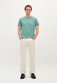 Turquoise cotton t-shirt with short sleeves, paired with cream wide-leg trousers and black shoes, standing against a neutral background.