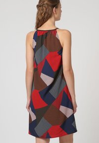 Un vestido sin mangas con un patrón geométrico en rojo, azul, marrón y gris, confeccionado con una tela texturizada y un diseño holgado.