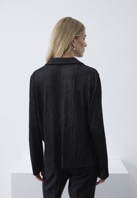 Giacca nera a righe metalliche con colletto, texture a costine e maniche lunghe, abbinata a pantaloni neri. Design semplice senza hardware visibile.