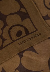 Καφέ υφασμάτινο σχέδιο με μεγάλα λουλουδένια μοτίβα και το όνομα της μάρκας «marimekko» τυπωμένο σε σκούρο καφέ. Λείο, απαλό υφή.