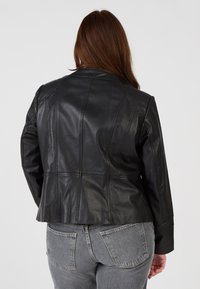 Schwarze Lederjacke mit tailliertem Design, ausgestattet mit mehreren Nahtdetails und einem leicht ausgestellten Saum, getragen über grauen Denim-Jeans.