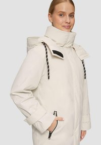 Witte outdoor jas met hoge kraag, ritszakken, contrasterende zwarte accenten en verstelbare trekkoorden. Glad, waterafstotend materiaal.