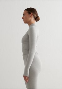 Top gris de manga larga hecho de un material liso y elástico. Presenta un escote alto y una silueta ajustada, que se extiende hasta las muñecas.