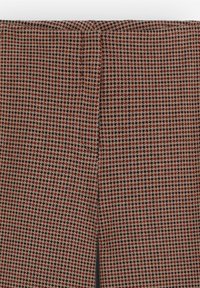 Tela con patrón de espiga en tonos marrón, crema y negro; textura suave con un corte recto y costuras mínimas.