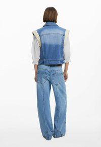 Denimweste mit einem hell- und dunkelblauen Farbverlauf, mit kontrastierendem Stoff an den Schultern. Locker sitzende hellblaue Jeans mit Gesäßtaschen.