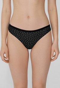 Schwarzer Bikiniunterteil mit weißen Punkten, ausgestattet mit einem weichen Bund. Der Stoff erscheint glatt und dehnbar, entworfen für Komfort.