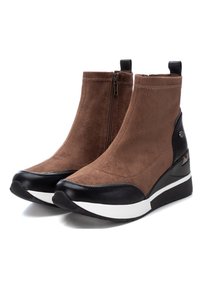 Botas de tobillo de ante marrón con punta y tacón de sintético negro. Cuentan con una cremallera lateral y una suela de cuña blanca y negra.