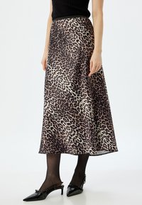 Falda midi de estampado de leopardo en tejido suave, con un diseño fluido. Combinada con tacones negros de tipo slingback y medias negras transparentes.
