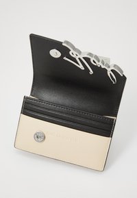 Zwart en crème leren portemonnee met zilverkleurige hardware, voorzien van kaarthouders en een designer logo accent. Soepele textuur en een strak design.