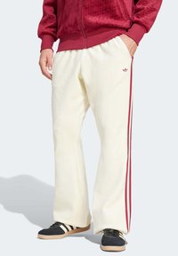 Kremfargede fleece joggebukser med røde sidekanter, med en avslappet passform og en brodert logo på lommen.