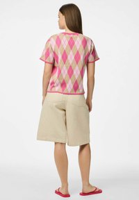 Krátký rukáv, pletený top s růžovým a béžovým kosočtvercovým vzorem. Kombinovaný s béžovými šortkami a růžovými žabkami, pohled zezadu.