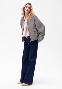 Tekstylna bomberka w wzór houndstooth w odcieniach szaro-czarnych, zestawiona z jasnoróżową bluzką i szerokimi ciemnoniebieskimi dżinsami. Buty w neutralnych kolorach.