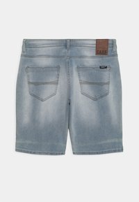 Shorts de mezclilla en azul claro con un aspecto desgastado. Cuenta con dos bolsillos traseros y una etiqueta de cuero marrón con la palabra 'CARS'. Diseño limpio.