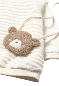 Top in tessuto bianco e texturizzato con una morbida tasca a forma di orsetto in beige, caratterizzata da dettagli facciali ricamati e accenti rosa; polsini a coste.