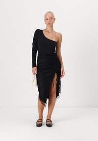 Μαύρο κορμάκι με έναν ώμο συνδυασμένο με μια μαύρη δαντελένια φούστα με ρυτίδες και πλαϊνό σκίσιμο. Τα αξεσουάρ περιλαμβάνουν μια μικρή λευκή τσάντα και μαύρες φλατ.