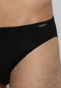 Zwarte geribde slips met een lage taille. Voorzien van een label met "AMMANN" op de tailleband. Glad textuur en aansluitende pasvorm.
