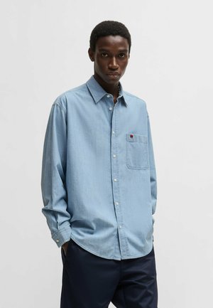 Light blue denim shirt with a button-down collar, single chest pocket, and white buttons. Smooth texture, relaxed fit, long sleeves.