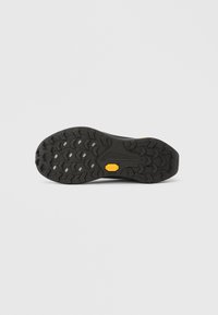 Suela de zapato de goma negra con un patrón de banda de rodadura multidireccional, que presenta ranuras prominentes y un logotipo amarillo de Vibram para una tracción mejorada.