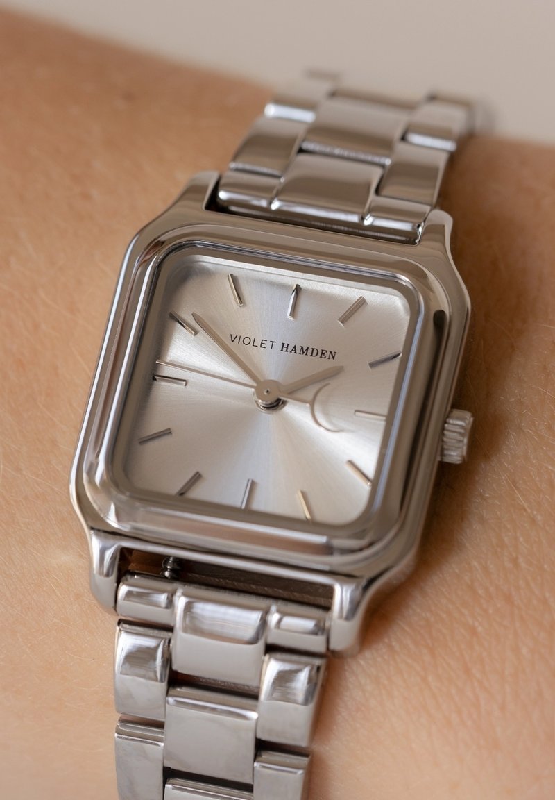 Silver stainless steel watch with a square face, textured silver dial, and stick markers. Features a polished bracelet and logo "VIOLET HAMDEN."