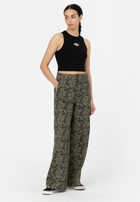 Débardeur noir court avec un petit logo blanc, associé à un pantalon vert ample avec un motif camouflage sombre, poches avant visibles.