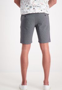 Pantaloni corti grigi realizzati in un materiale morbido, lunghi fino al ginocchio con una vestibilità classica, dotati di due tasche posteriori e una texture liscia. Sono indossate delle scarpe bianche.