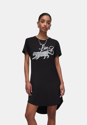 Mujer que lleva un vestido negro de manga corta con un gráfico de leopardo blanco y el texto "Liu Jo" en la parte delantera, complementado con joyas de plata.