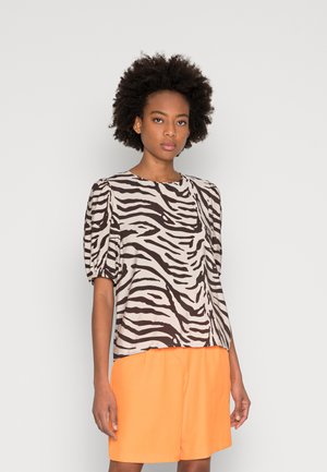 Blusa de manga curta em bege com riscas de zebra pretas, com um decote redondo e mangas ligeiramente bufantes, combinada com calções laranja.