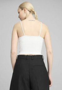 Hvid ribbet crop top med tynde stropper, parret med højtaljede sorte bukser med en baglomme og bælteholdere. Glat tekstur.
