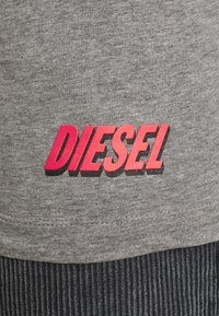 Tissu gris à finition texturée, avec un logo "DIESEL" audacieux en lettres rose et noires près de l'ourlet. Design simple et décontracté.