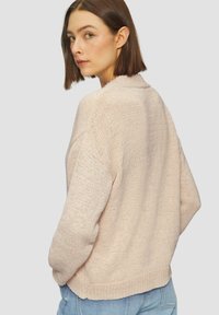 Pull en tricot rose clair avec une coupe décontractée, épaules tombantes et ourlet côtelé. Présente un tissu texturé et respirant.