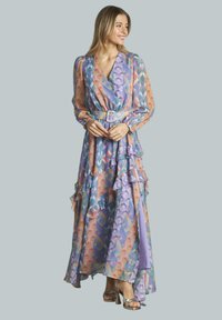 Langes, fließendes Kleid in helllila mit bunten geometrischen Mustern. Mit Rüschen, einem gebundenen Gürtel und langen Ärmeln; leichtes Material.