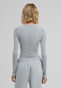 Langermet grå topp med en tettsittende design, laget av mykt stoff. Har en rund hals og jevn tekstur, kombinert med grå joggebukser.