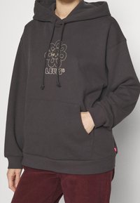 Felpa con cappuccio in cotone grigio scuro con tasca frontale, caratterizzata da un vivace motivo floreale e cordini per la regolazione.